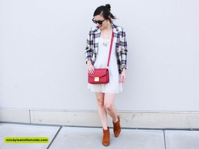 A woman in a white dress and plaid jacket holds a red purse, showcasing a stylish hipster outfit.