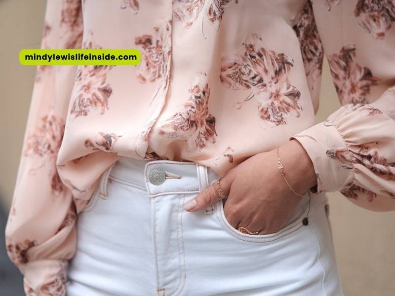 A woman dressed in white jeans and a pink floral blouse exudes a cheerful and trendy vibe in her outfit.