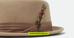 A tan pork pie hat adorned with a decorative feather on the side.