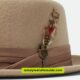 A tan pork pie hat adorned with a decorative feather on the side.