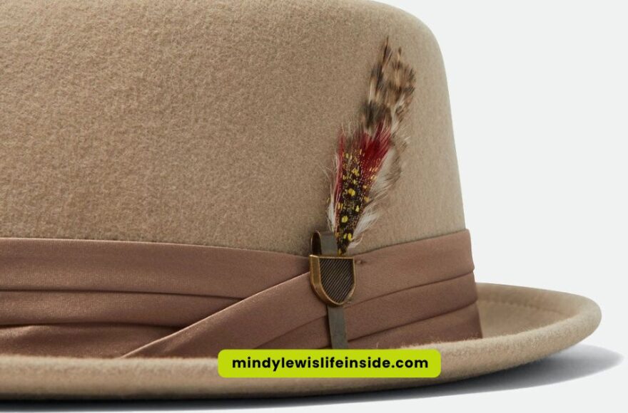 A tan pork pie hat adorned with a decorative feather on the side.
