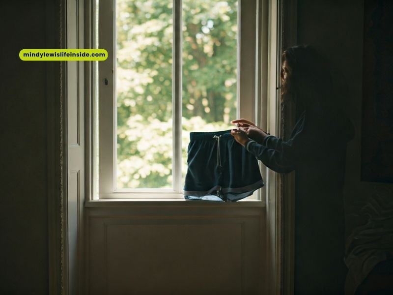 A woman looks out the window with a bag, pondering her outfit choice for tomorrow's weather.