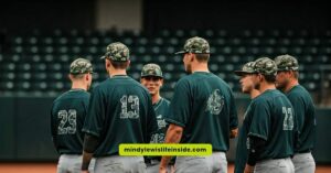 Baseball players in green uniforms engage in conversation, showcasing their camouflage hats during a themed game.
