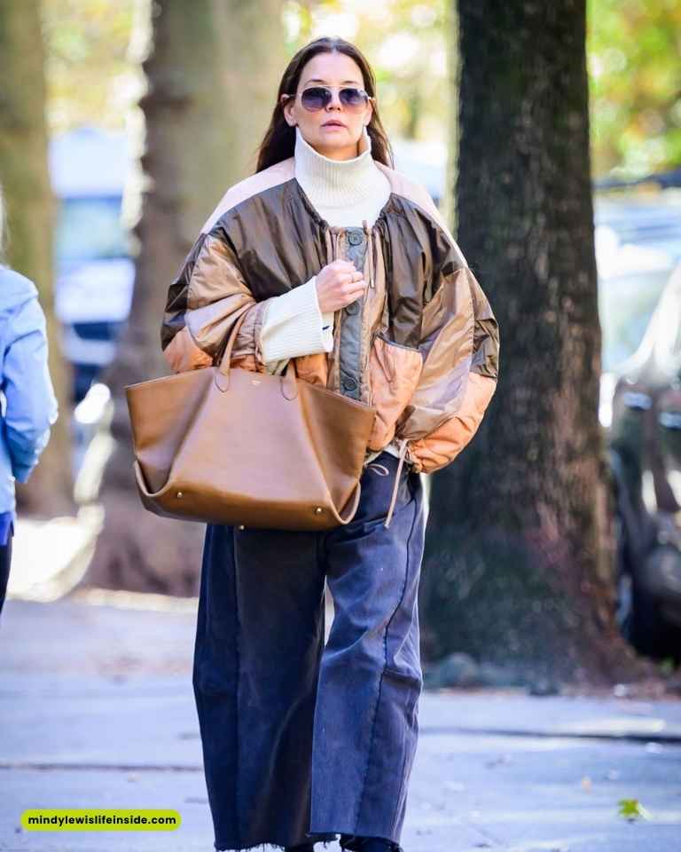 A woman in a brown jacket and wide pants walks confidently down the street.