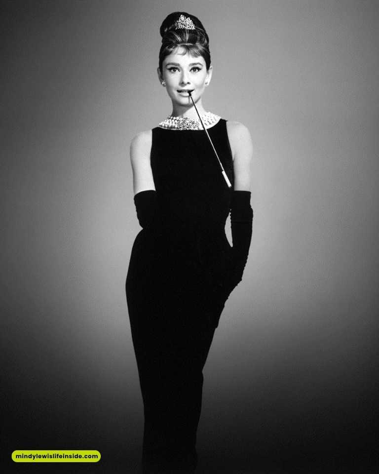 Audrey Hepburn in an elegant black dress, holding a cigarette, exuding classic Hollywood glamour at a celebrity event.