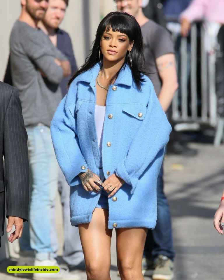 Rihanna wearing a blue coat and shorts, confidently walking on the street at a celebrity event.
