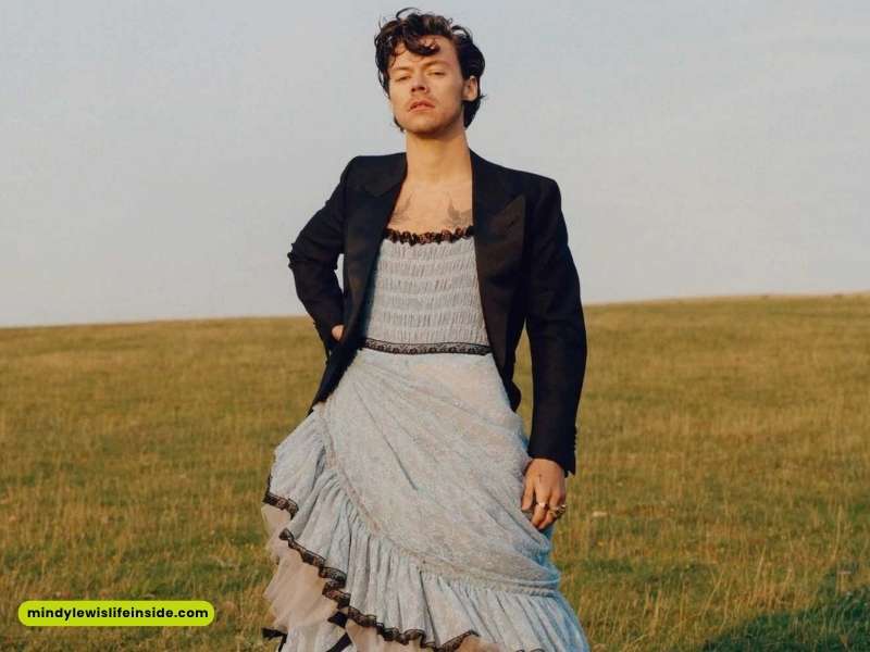 A man in a blue dress stands amidst a field, representing a bold fashion choice for a celebrity event.