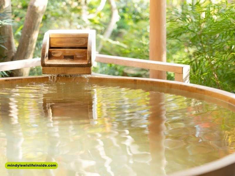 A wooden bath tub with water cascading over the edge, evoking a tranquil onsen atmosphere.