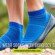Blue socks are paired with black barefoot shoes on a pebble path. Text reads, "Do you wear socks with barefoot shoes?" The background is blurred greenery.