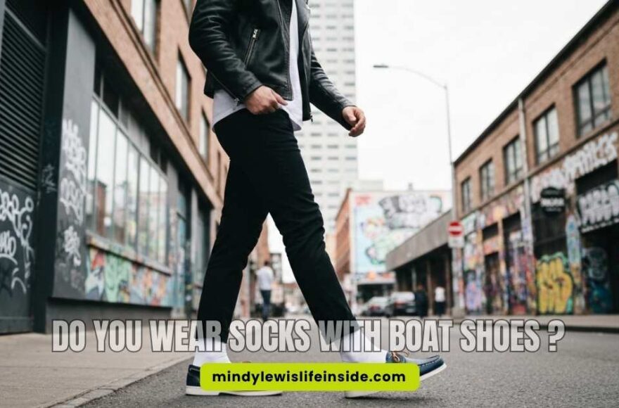 A person in a leather jacket walks down a graffiti-filled urban street, wearing black pants and blue loafers, conveying a trendy and casual vibe.